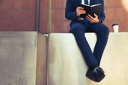 Businessman's body in suit seated in metal wall reading with cof_111391151_XS